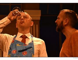 Spektakl „Kolacja dla głupca” - dwaj mężczyźni, jeden pije z kieliszka, drugi patrzy w jego stronę