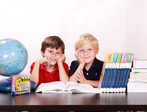 Chłopcy przy biurku na którym są książki i globus fot. pixabay