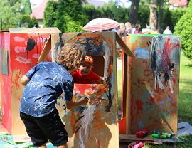 dwaj chłopcy bawią sie w pomalowanych kolorowymi farbami kartonowych pudełkach