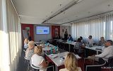 Spotkanie robocze w ramach Miejskiego Obszaru Funkcjonalnego Krosno. Zdjęcie przedstawia osoby obradujące w sali konferencyjnej. Na ekranie wyświetlana jest prezentacja.